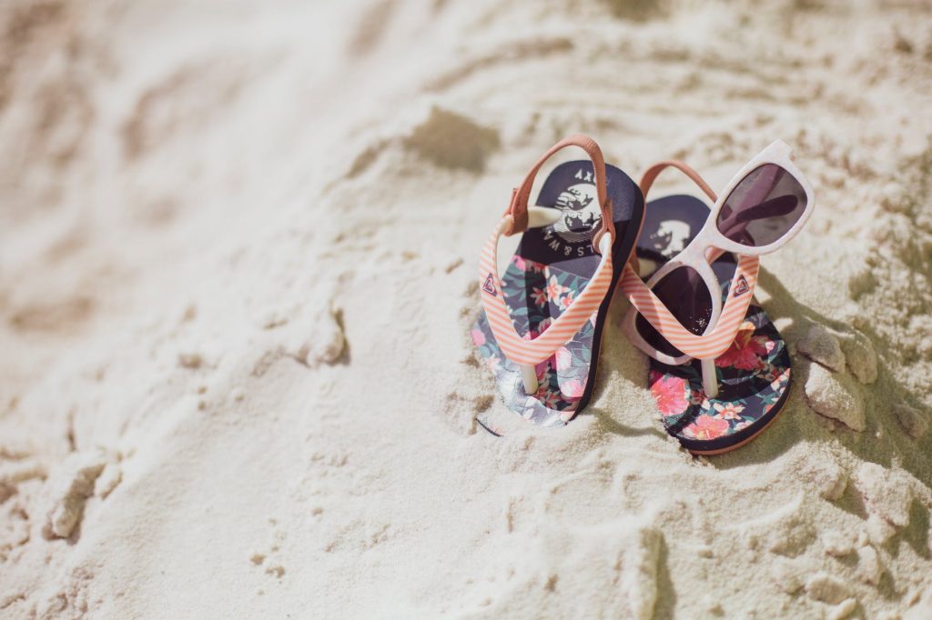 Child's flip flops and sunglasses on sand.