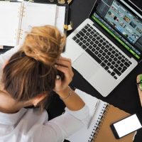woman with head in hands sitting in front of a laptop