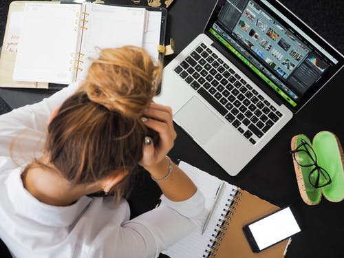 woman with head in hands sitting in front of a laptop