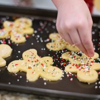 child's hand decorating cookies with sprinkles