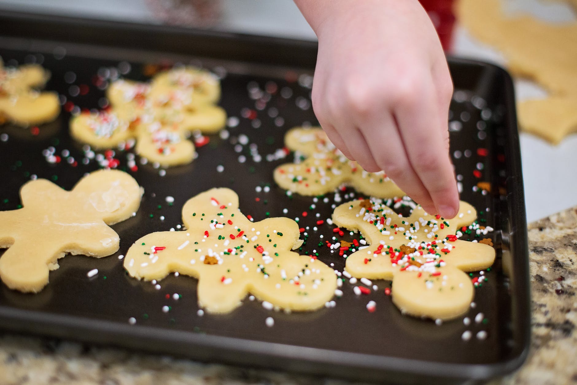 child's hand decorating cookies with sprinkles