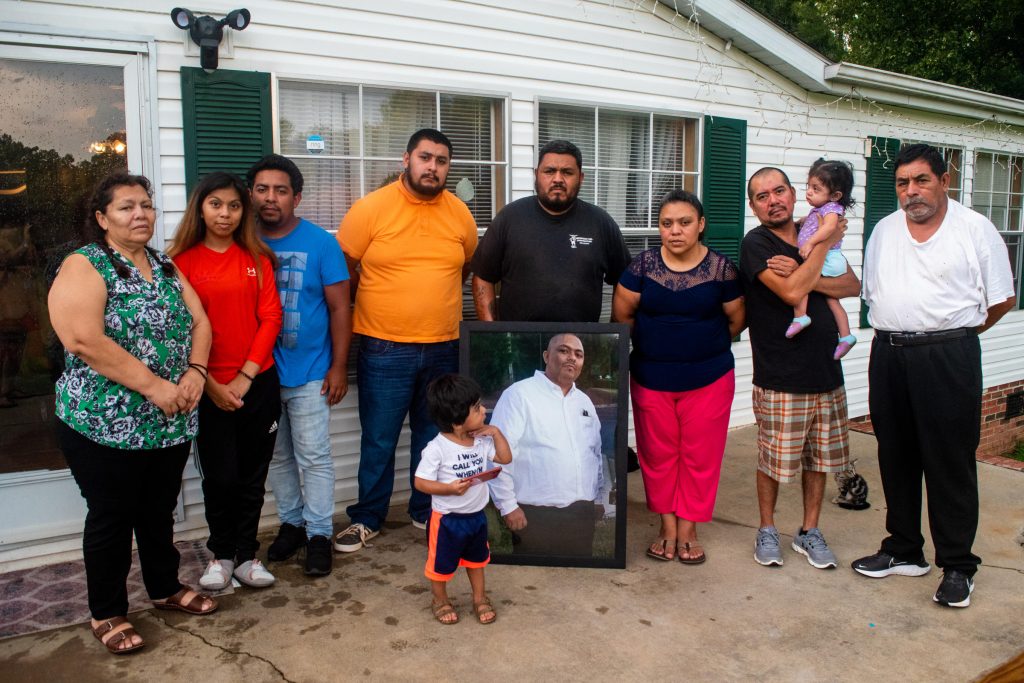 Members of the Chagoyan family stand outside their home in Midland, North Carolina, holding a portrait of Juan Chagoyan, who died July 20. LAURA BRACHE, WFAE