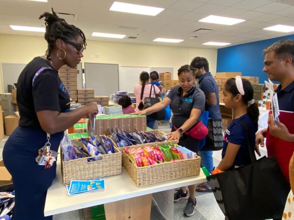 Assistant Principal Imani Harper (left) helps families choose supplies at a CMS back-to-school bash held at Renaissance West Aug. 12.